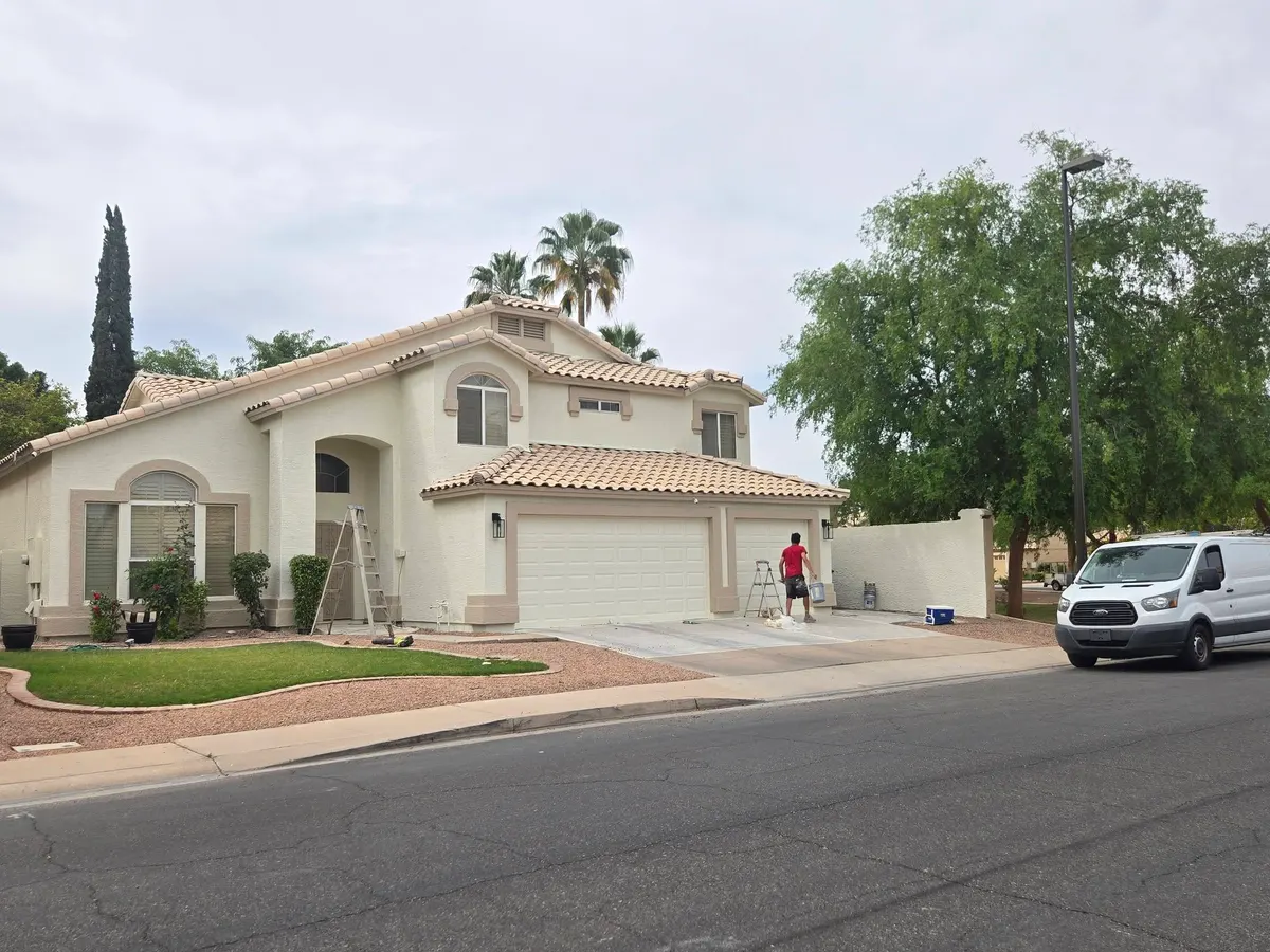 Painter working on garage doors and trim of a white stucco home
